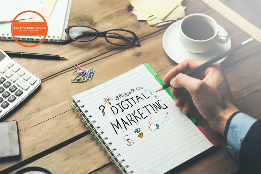 Luxe Drive Digital Marketing America's Top Marketing Agency A person writing "Digital Marketing" in a notebook on a desk, surrounded by a laptop, calculator, coffee cup, and stationery. Luxe Drive Digital Marketing We Drive Your Growth