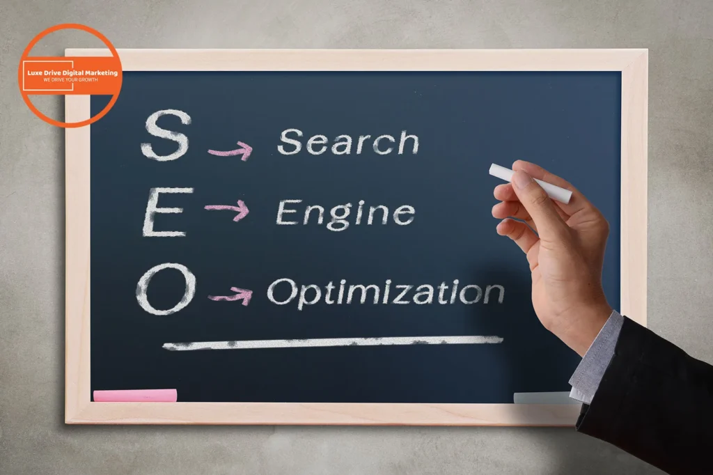 Luxe Drive Digital Marketing America's Top Marketing Agency Hand writing on a chalkboard displaying the words "Search," "Engine," and "Optimization," with arrows pointing from "SEO. Luxe Drive Digital Marketing We Drive Your Growth
