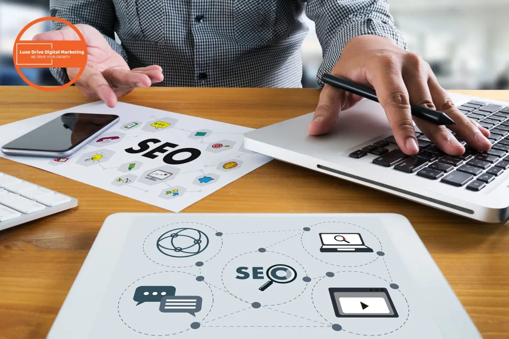 Luxe Drive Digital Marketing America's Top Marketing Agency Person working on SEO strategy with electronic devices and printed materials on a wooden desk. Luxe Drive Digital Marketing We Drive Your Growth