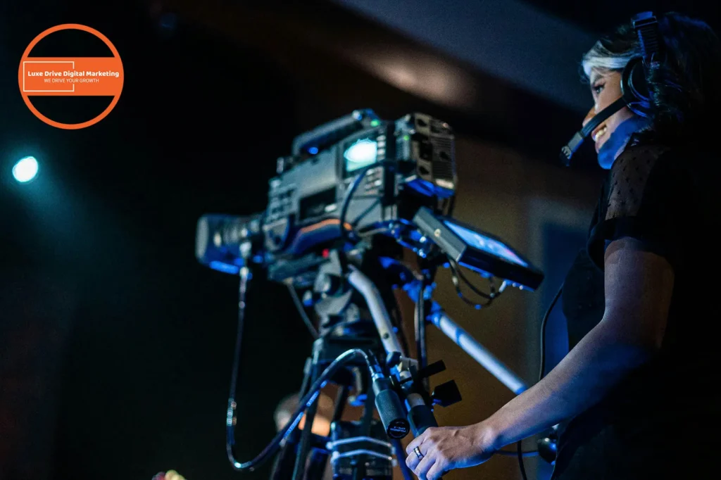 Luxe Drive Digital Marketing America's Top Marketing Agency Camera operator with headset focuses on filming in a dimly lit setting. A logo for "Luxe Drive Digital Marketing" is visible in the corner. Luxe Drive Digital Marketing We Drive Your Growth