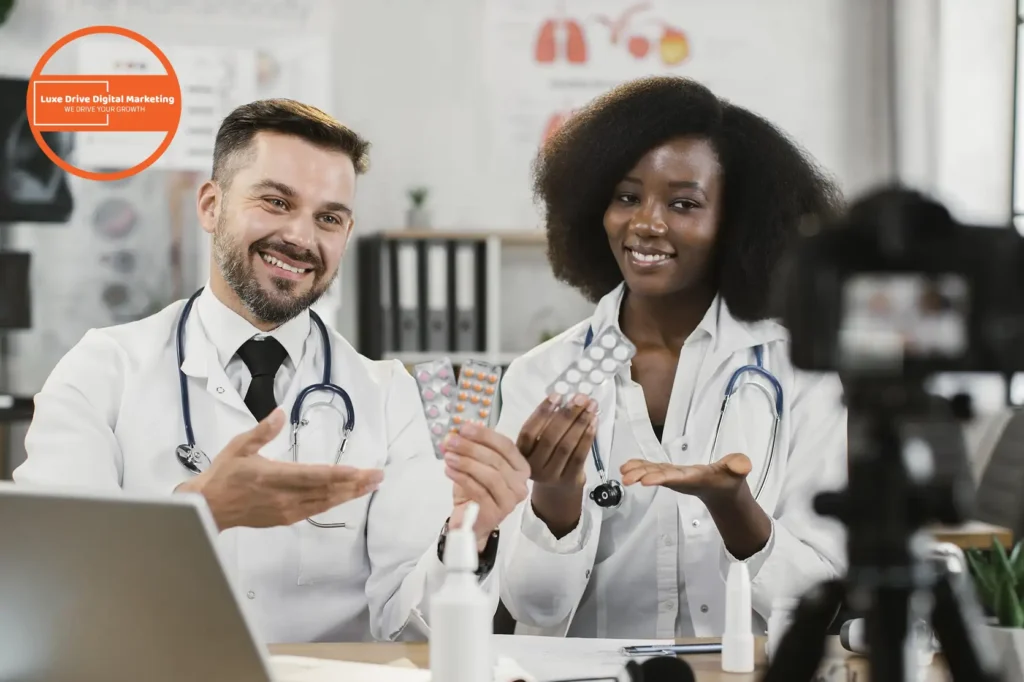 Luxe Drive Digital Marketing America's Top Marketing Agency Two doctors smiling and holding medication blister packs, seated in an office with medical charts in the background. Luxe Drive Digital Marketing We Drive Your Growth
