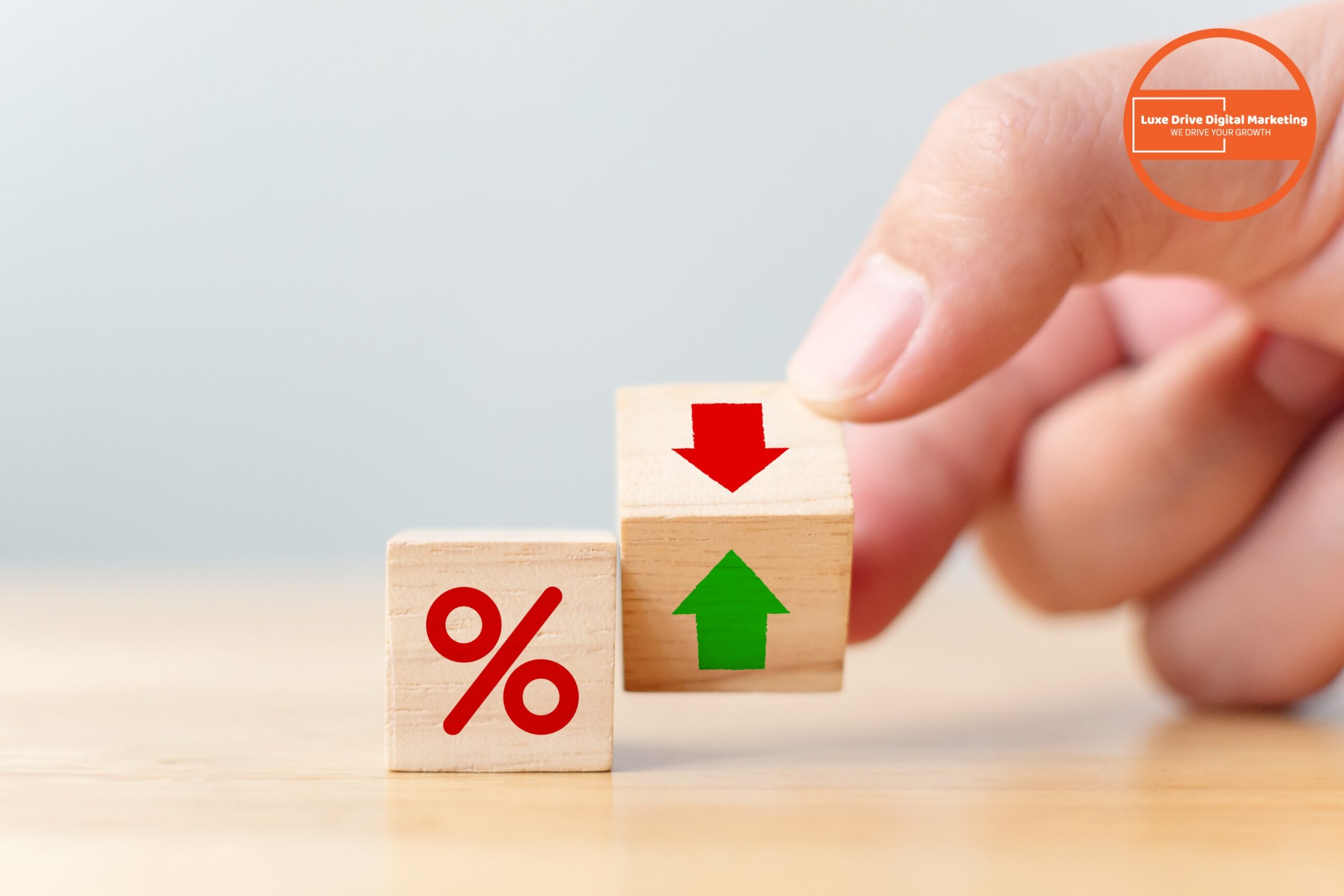 Luxe Drive Digital Marketing America&#039;s Top Marketing Agency A hand turns wooden blocks displaying a red percent sign, a red down arrow, and a green up arrow on a light surface. Luxe Drive Digital Marketing We Drive Your Growth