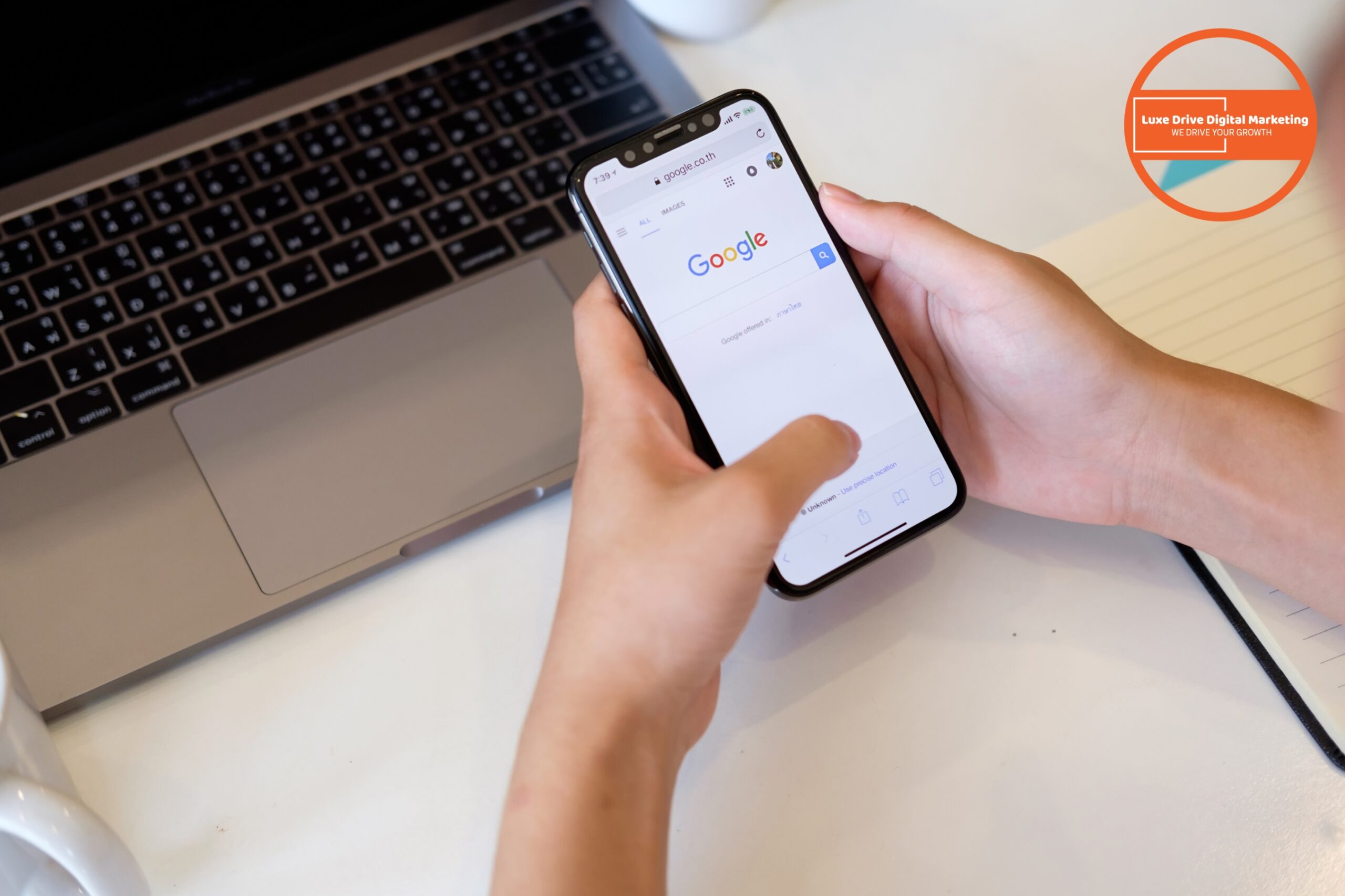 Luxe Drive Digital Marketing America&#039;s Top Marketing Agency A person uses a smartphone to browse Google next to a laptop, notebook, and a coffee cup on a white desk. An orange &quot;Luxe Drive Digital Marketing&quot; logo appears in the corner. Luxe Drive Digital Marketing We Drive Your Growth