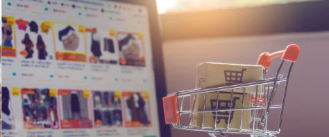 Luxe Drive Digital Marketing America's Top Marketing Agency A small shopping cart with a cardboard box inside is in front of a computer screen displaying various online shopping items. Luxe Drive Digital Marketing We Drive Your Growth